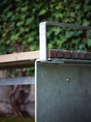 A close up image of a park bench detailing the wood, the steel and the armrest that makes up the bench.